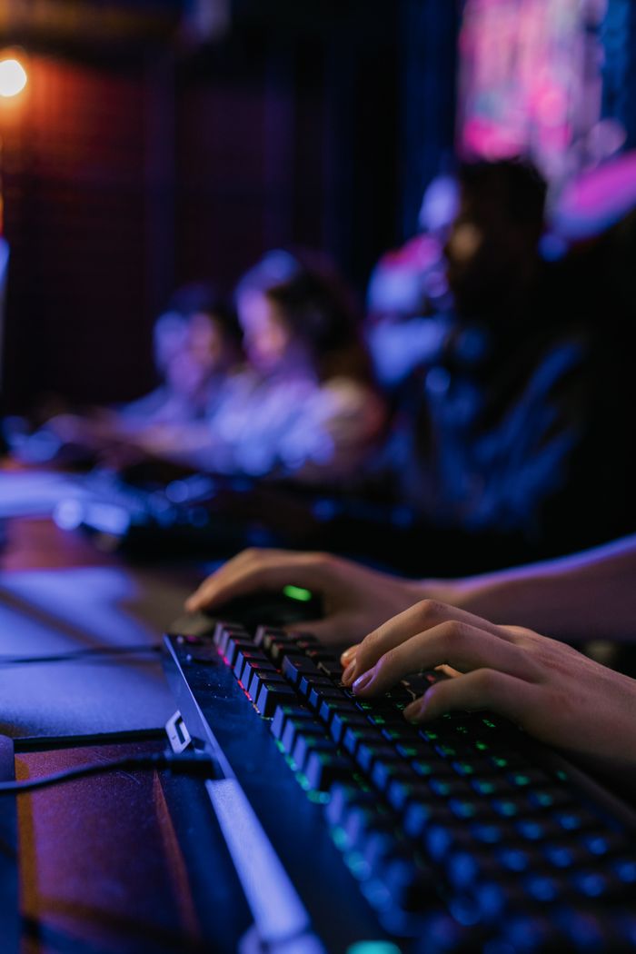 Tienda Oficial PCMR Close-up of hands on keyboard during a multiplayer gaming session in dimly lit room.